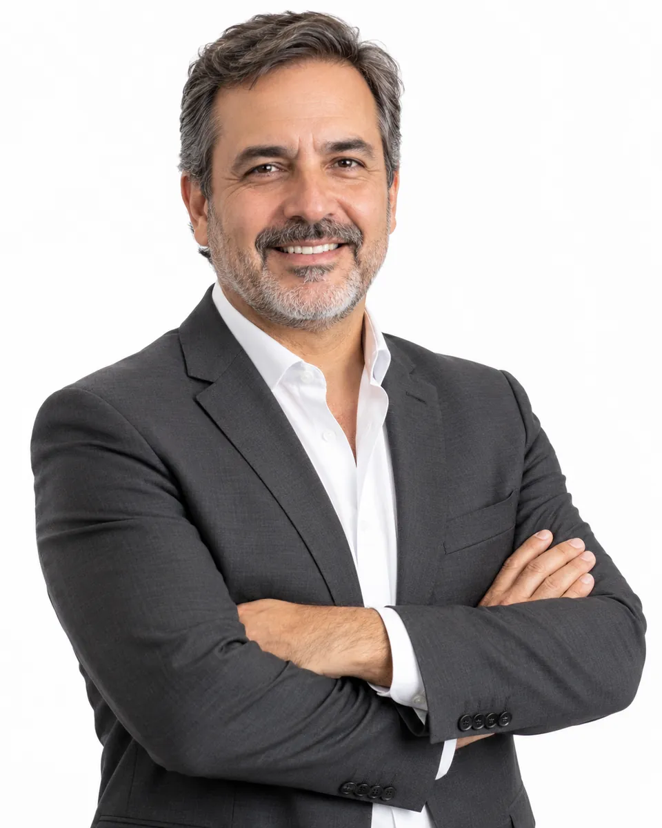 Retrato profesional de medio cuerpo de un director con brazos cruzados, saco gris y fondo blanco.
